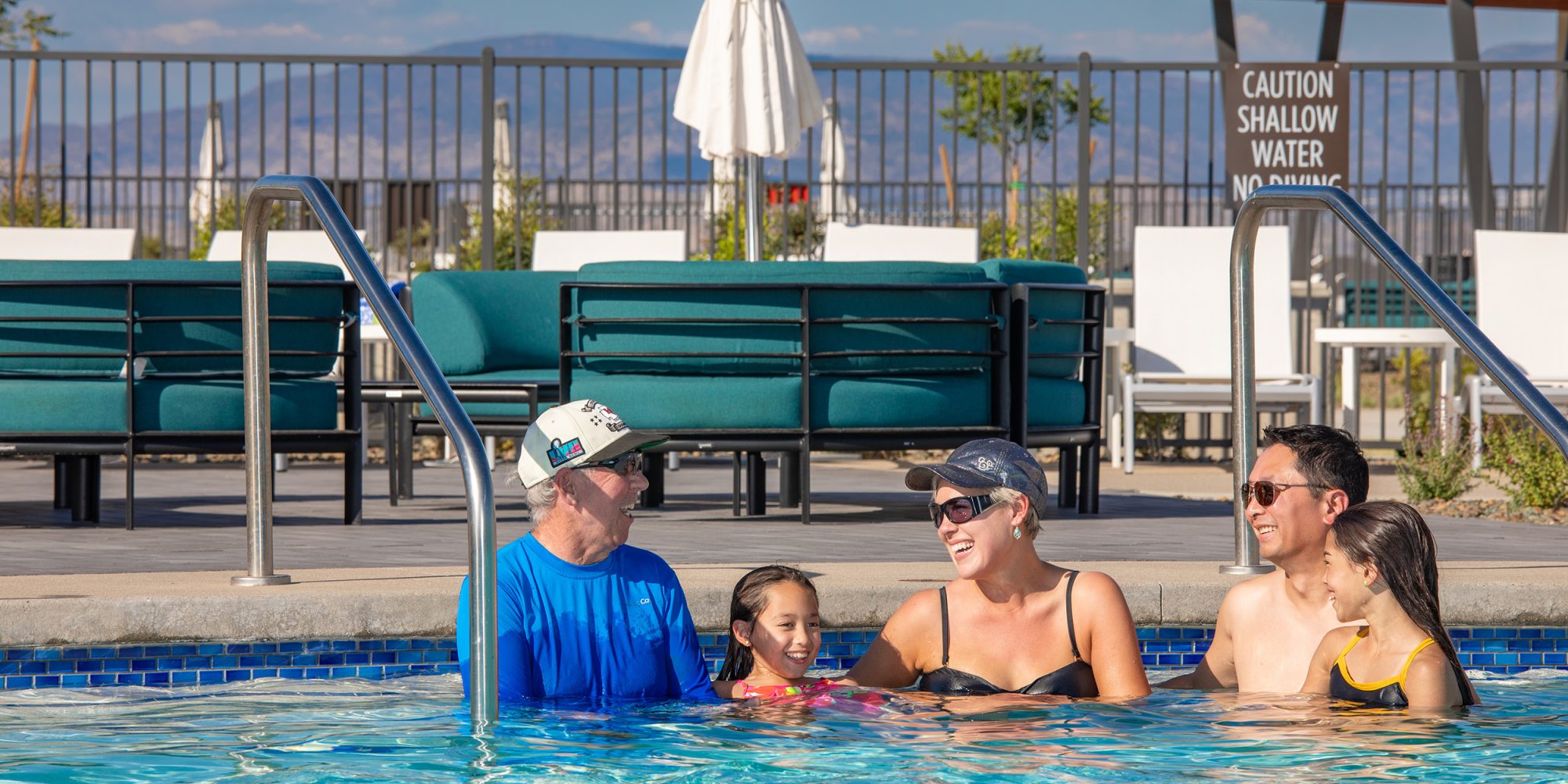two young girls in the pool with their parents and grandfather laughing